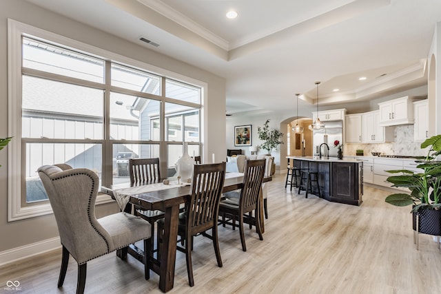 dining room featuring arched walkways, a raised ceiling, visible vents, and light wood-style flooring