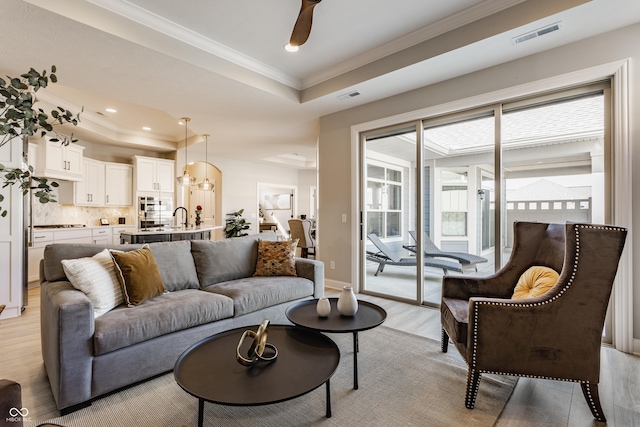 living area with a tray ceiling, light wood-type flooring, visible vents, and crown molding