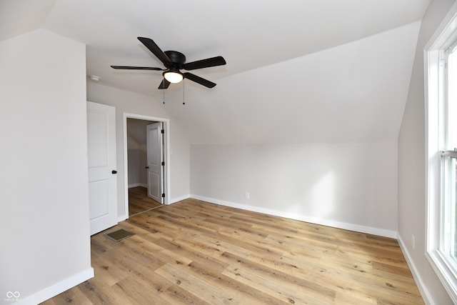 additional living space with light wood-style flooring, visible vents, a ceiling fan, vaulted ceiling, and baseboards