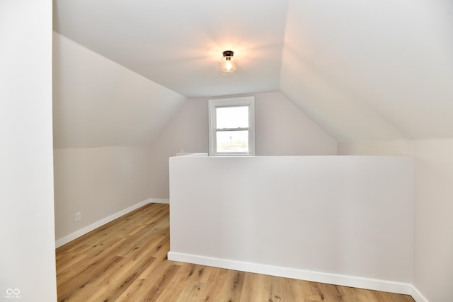 additional living space featuring vaulted ceiling, light wood-style flooring, and baseboards