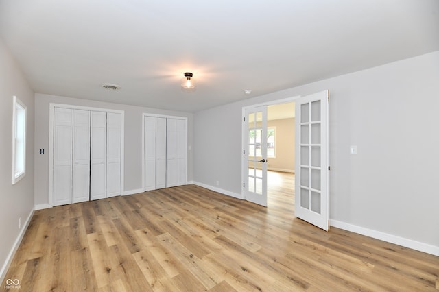 unfurnished bedroom featuring french doors, multiple closets, visible vents, light wood-type flooring, and baseboards