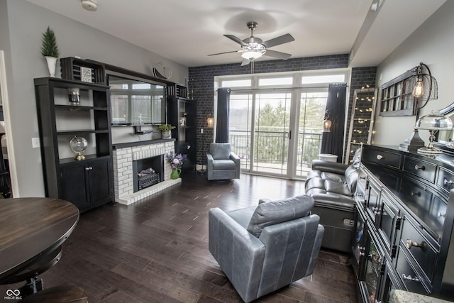 living area with a brick fireplace, ceiling fan, brick wall, and wood finished floors