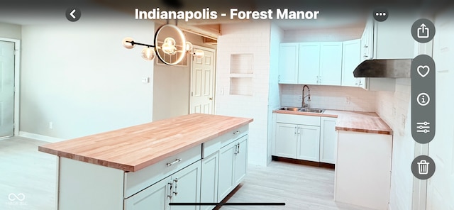 kitchen with tasteful backsplash, butcher block counters, light wood-type flooring, under cabinet range hood, and a sink