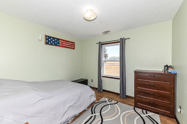 bedroom with wood finished floors, visible vents, and baseboards