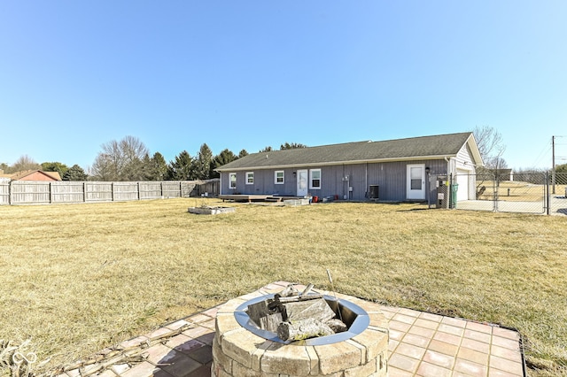 back of house with a garage, fence private yard, a lawn, and a fire pit