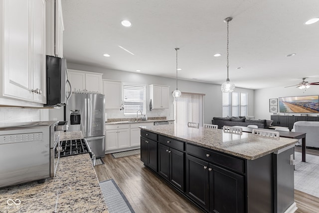 kitchen featuring appliances with stainless steel finishes, white cabinetry, a sink, a kitchen island, and dark cabinetry