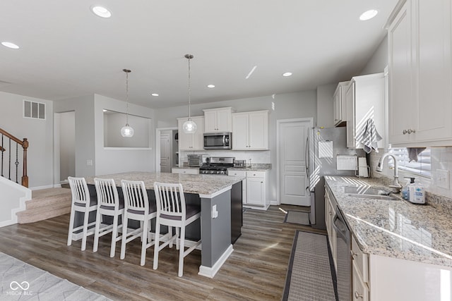 kitchen with stainless steel appliances, visible vents, a kitchen island, a sink, and a kitchen breakfast bar