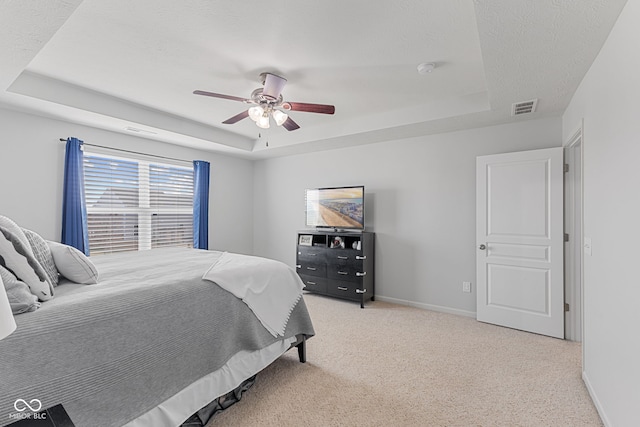 carpeted bedroom featuring a tray ceiling, a ceiling fan, visible vents, and baseboards