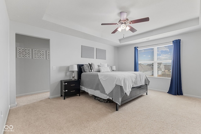 carpeted bedroom featuring a tray ceiling, ceiling fan, and baseboards