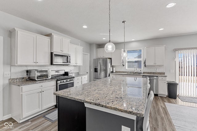 kitchen with light wood-style flooring, stainless steel appliances, white cabinetry, a center island, and tasteful backsplash