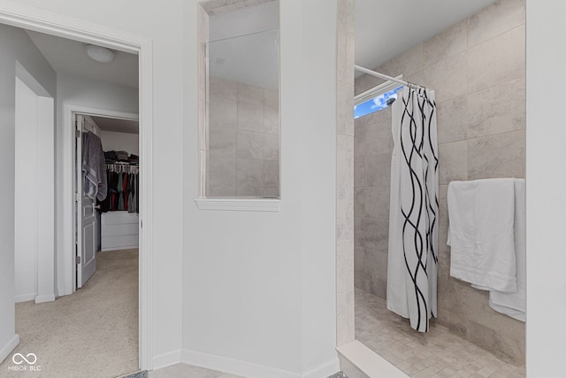 bathroom with a tile shower, a spacious closet, and baseboards