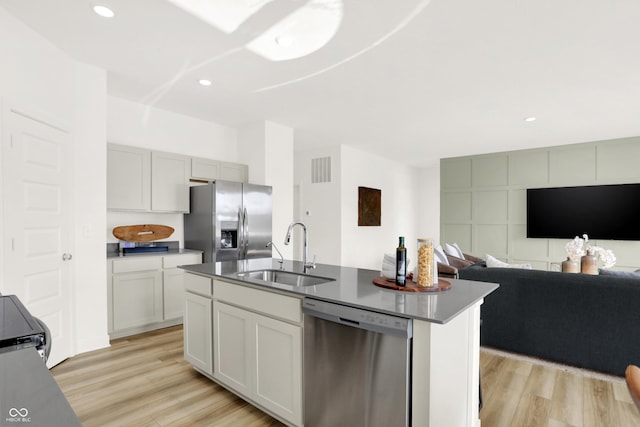 kitchen with light wood finished floors, appliances with stainless steel finishes, open floor plan, and a sink