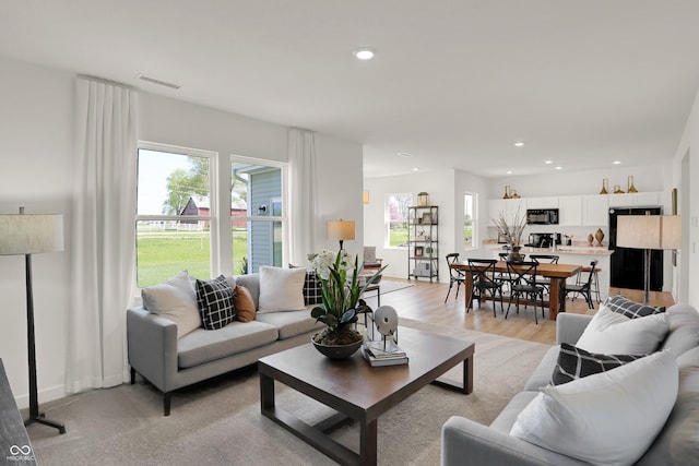 living room with light wood-type flooring, plenty of natural light, visible vents, and recessed lighting