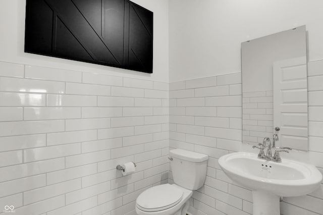 half bath featuring a sink, toilet, and tile walls