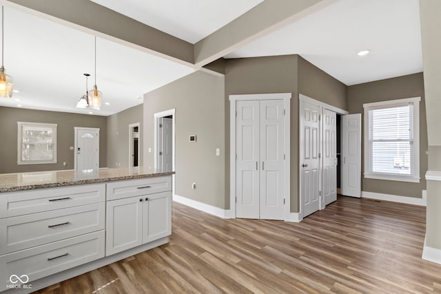 kitchen with white cabinets, hanging light fixtures, light wood finished floors, baseboards, and light stone countertops