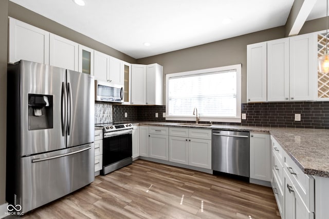 kitchen featuring backsplash, appliances with stainless steel finishes, light wood-style floors, white cabinets, and a sink