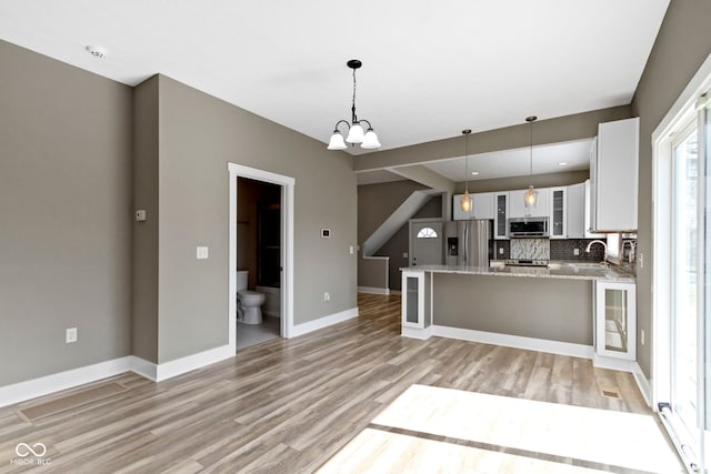 kitchen featuring light wood-type flooring, tasteful backsplash, appliances with stainless steel finishes, glass insert cabinets, and a chandelier