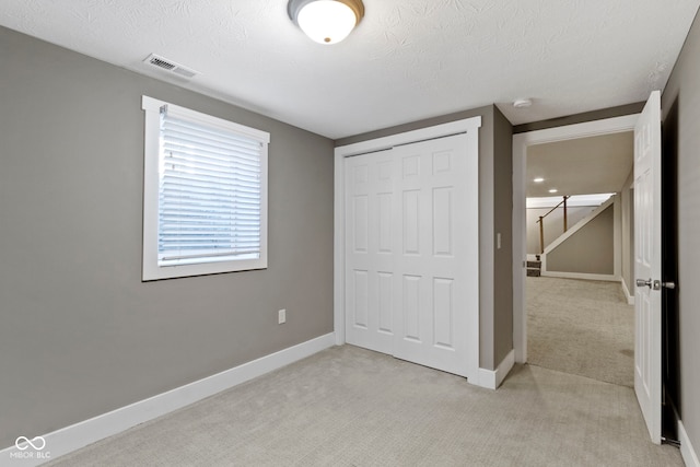 unfurnished bedroom with light carpet, visible vents, baseboards, and a closet