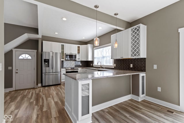 kitchen with a peninsula, glass insert cabinets, wood finished floors, and stainless steel appliances