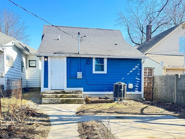 exterior space with entry steps, central AC unit, a shingled roof, and fence