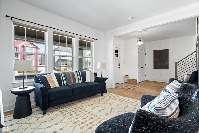 living area with baseboards, an inviting chandelier, wood finished floors, and stairs