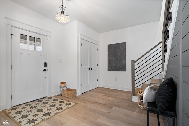 foyer entrance featuring baseboards, an inviting chandelier, stairs, and light wood finished floors