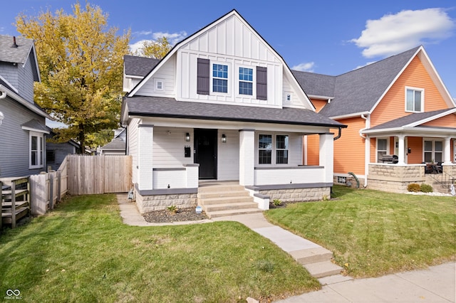 view of front of home featuring fence, covered porch, a shingled roof, a front lawn, and board and batten siding