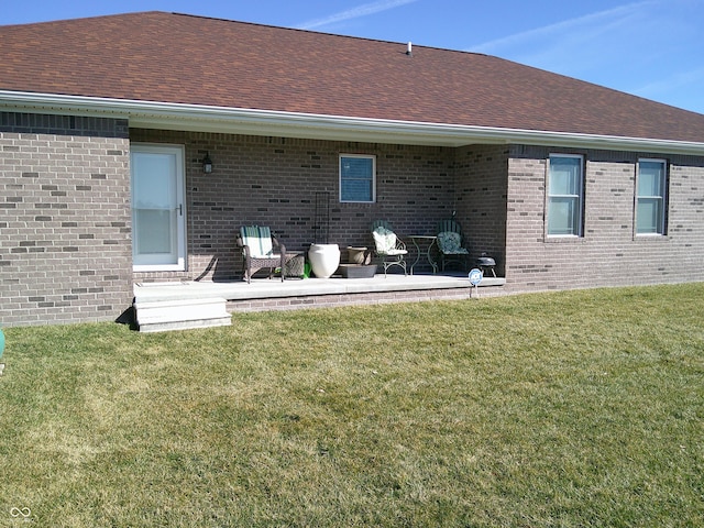 back of property with a shingled roof, brick siding, a lawn, and a patio