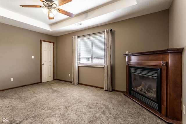 unfurnished living room with a tray ceiling, visible vents, a glass covered fireplace, light carpet, and baseboards