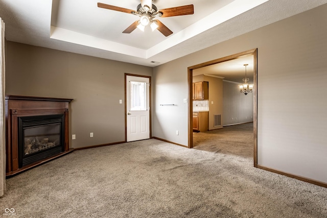 unfurnished living room with a tray ceiling, light colored carpet, visible vents, a glass covered fireplace, and baseboards