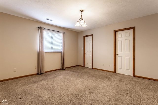 empty room featuring light carpet, visible vents, baseboards, a textured ceiling, and a chandelier