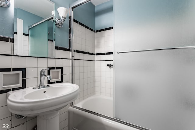 full bath with a sink, tile walls, and bath / shower combo with glass door