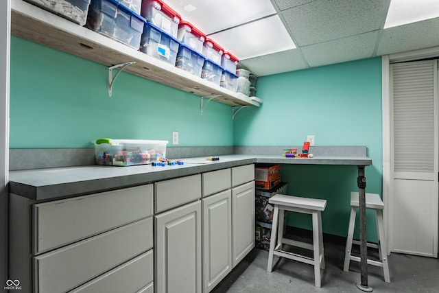 kitchen featuring white cabinets, a drop ceiling, light countertops, concrete flooring, and open shelves