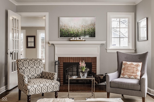 living area with ornamental molding, a brick fireplace, wood finished floors, and baseboards