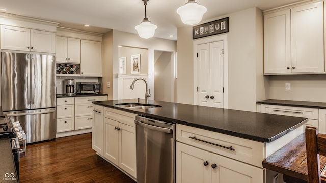 kitchen featuring dark wood-style floors, decorative light fixtures, dark countertops, appliances with stainless steel finishes, and a sink