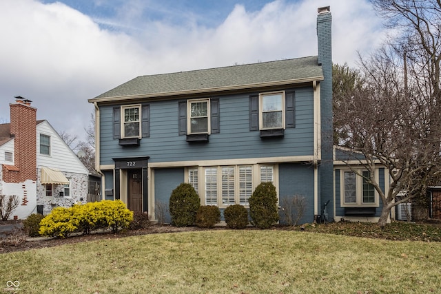 colonial house with roof with shingles, a chimney, a front lawn, and brick siding