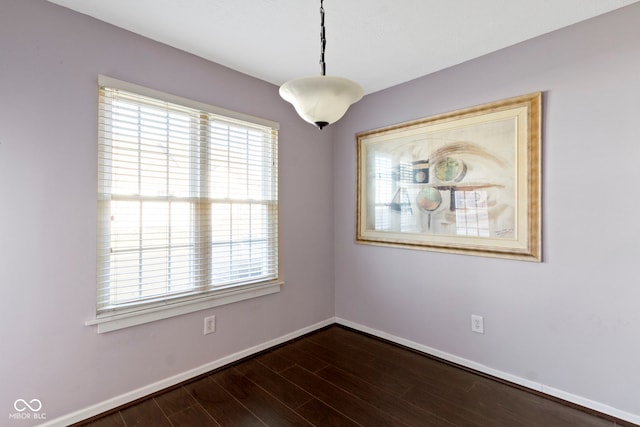 empty room featuring baseboards, dark wood-style flooring, and a wealth of natural light