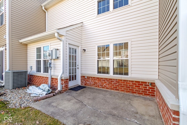 entrance to property with central AC, brick siding, and a patio area