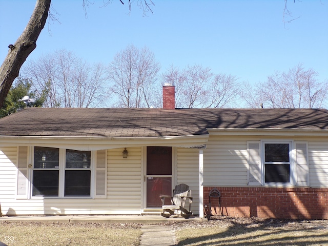 ranch-style house featuring brick siding, roof with shingles, and a chimney