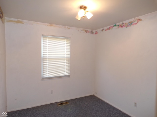 unfurnished room with baseboards, visible vents, and dark carpet