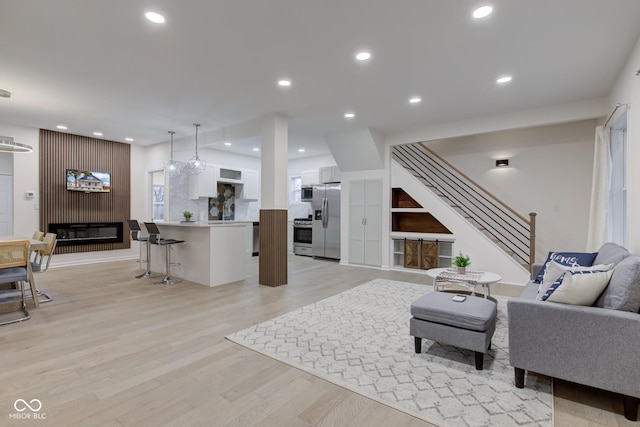 living room with recessed lighting, a fireplace, stairway, and light wood finished floors