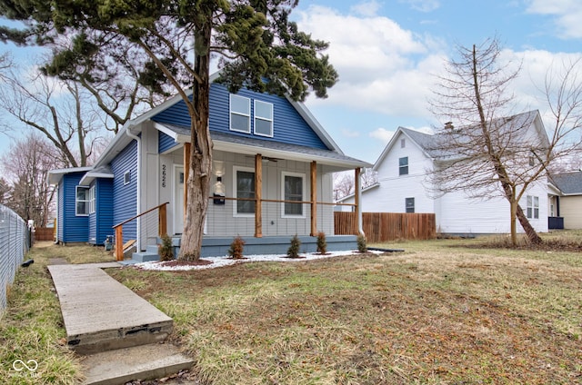 bungalow-style home featuring covered porch, a front lawn, board and batten siding, and fence