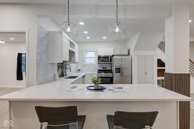 kitchen with appliances with stainless steel finishes, a peninsula, a sink, light countertops, and backsplash