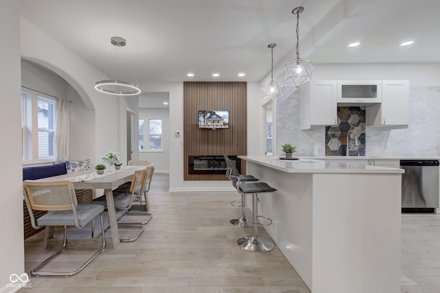 kitchen with white cabinets, light wood finished floors, backsplash, and dishwasher