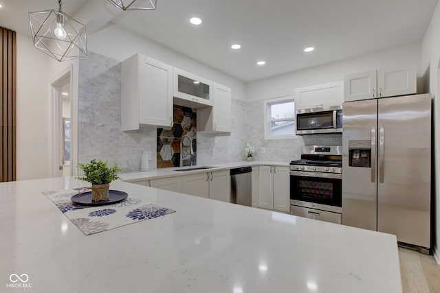 kitchen with light stone counters, appliances with stainless steel finishes, a sink, white cabinetry, and backsplash