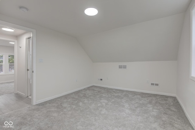 additional living space with carpet, visible vents, vaulted ceiling, and baseboards