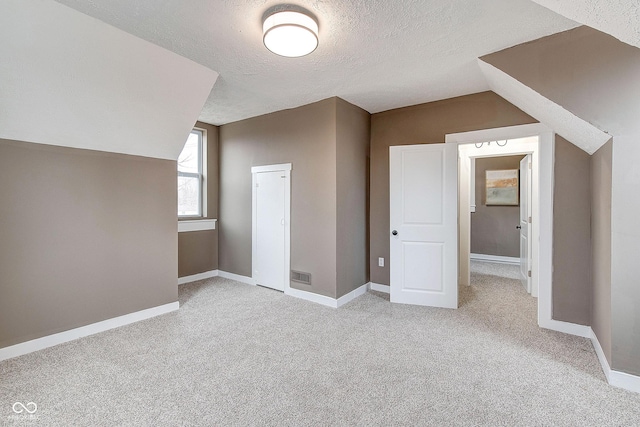 bonus room featuring vaulted ceiling, a textured ceiling, light carpet, and visible vents