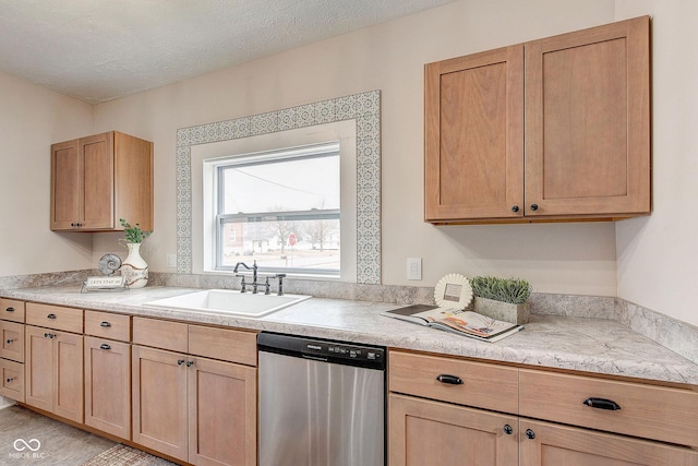 kitchen featuring light countertops, a textured ceiling, stainless steel dishwasher, light brown cabinets, and a sink