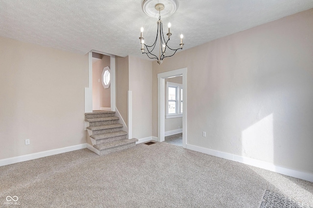 carpeted empty room featuring a textured ceiling, stairway, and baseboards