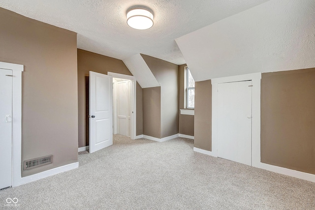 additional living space featuring carpet floors, visible vents, a textured ceiling, and lofted ceiling